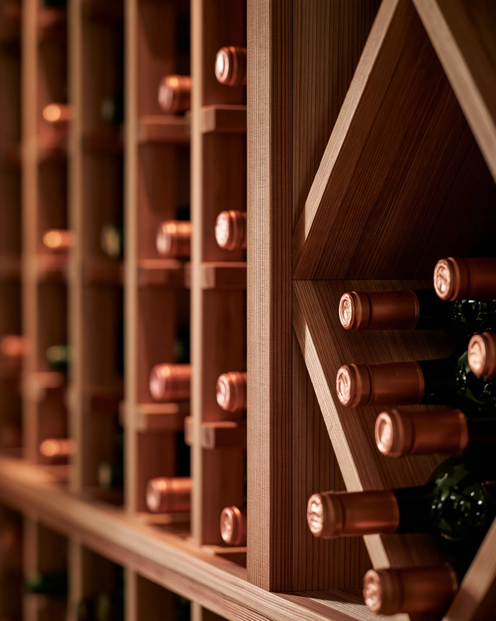 Close view of wood racking with foil-capped bottle necks in individual slots beside a diamond bin